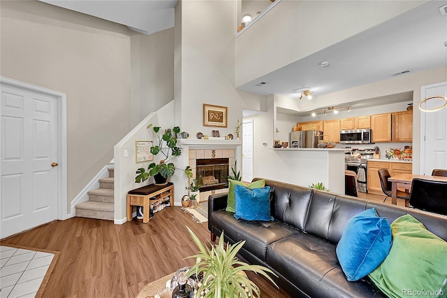 living room with light wood-type flooring, stairs, track lighting, baseboards, and a tile fireplace