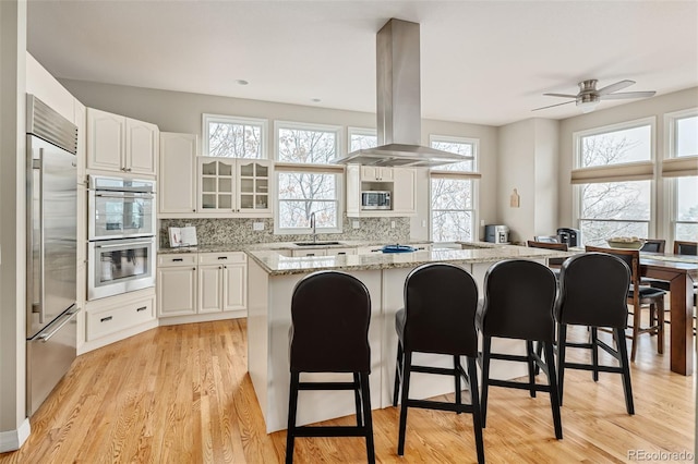 kitchen with a kitchen island, built in appliances, a breakfast bar area, island range hood, and a sink