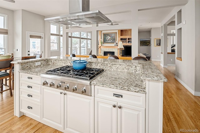 kitchen featuring stainless steel gas cooktop, open floor plan, wall chimney exhaust hood, and light stone counters