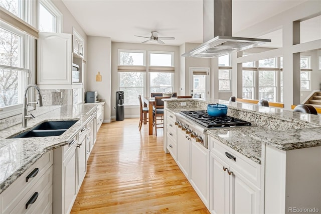 kitchen with a kitchen island, island exhaust hood, light wood-style floors, stainless steel gas stovetop, and a sink