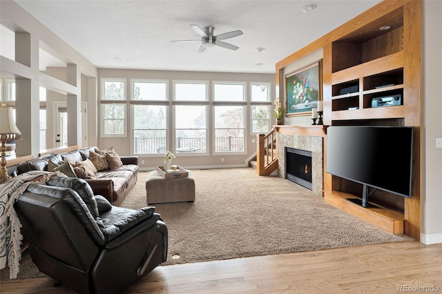 living room featuring baseboards, wood finished floors, a ceiling fan, and a tile fireplace