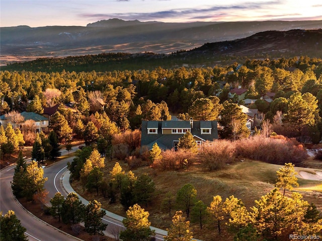 aerial view at dusk featuring a mountain view and a view of trees