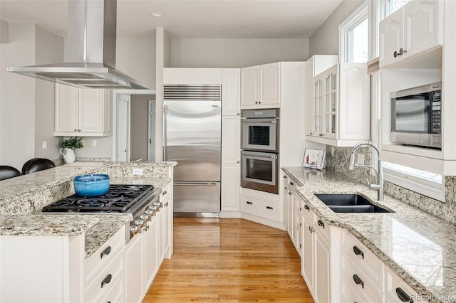 kitchen featuring light wood finished floors, glass insert cabinets, extractor fan, built in appliances, and a sink