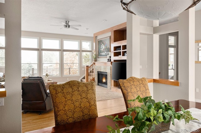 living area featuring a ceiling fan, a textured ceiling, wood finished floors, and a tile fireplace