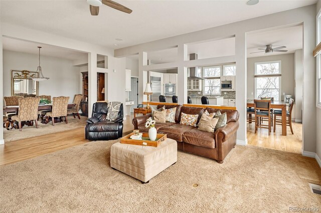 carpeted living area with visible vents, baseboards, ceiling fan, and wood finished floors