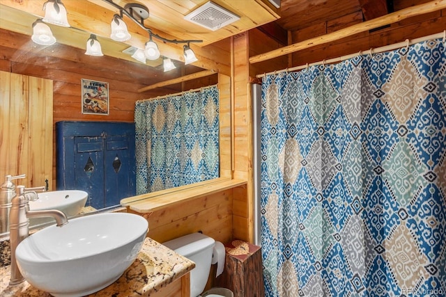 bathroom featuring curtained shower, wooden walls, sink, and toilet