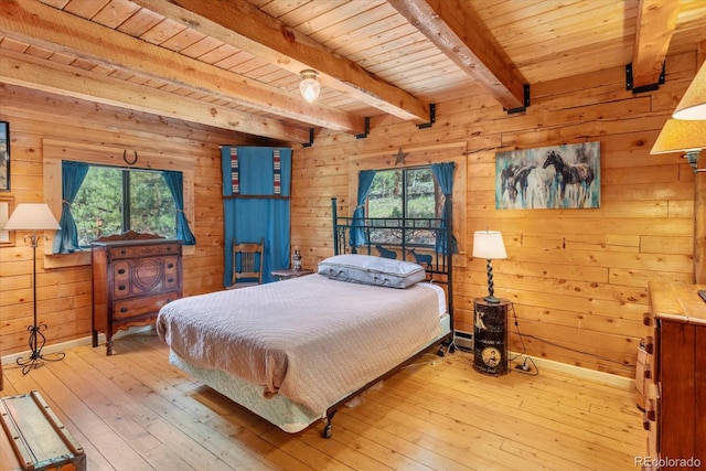 bedroom with multiple windows, wood walls, beamed ceiling, and light wood-type flooring