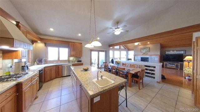 kitchen with a fireplace, stainless steel appliances, ceiling fan, a center island with sink, and sink