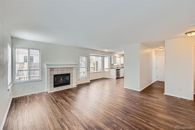 unfurnished living room featuring a tiled fireplace and dark hardwood / wood-style floors