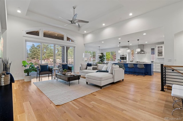 living room with ceiling fan, a towering ceiling, and light hardwood / wood-style flooring