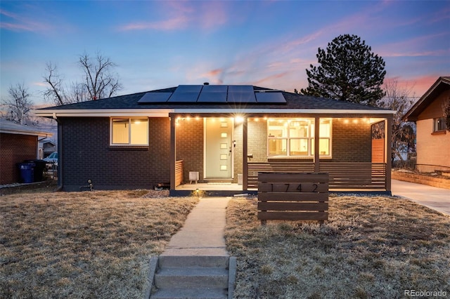 bungalow-style house featuring roof mounted solar panels, a front lawn, and brick siding