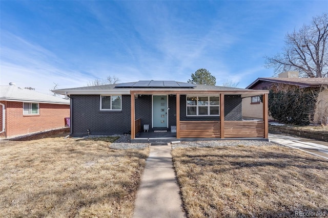 view of front of property featuring a front yard, a porch, solar panels, and brick siding