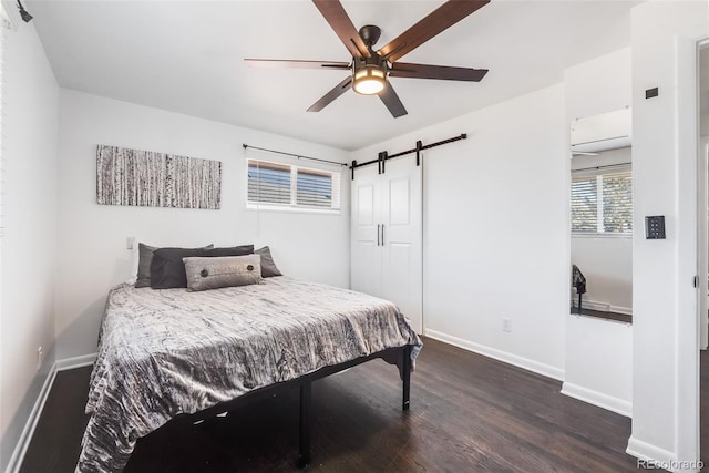 bedroom featuring dark wood-style floors, a barn door, baseboards, and ceiling fan