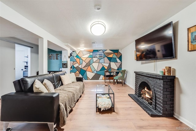 living room featuring an accent wall, a brick fireplace, light wood-style flooring, and baseboards