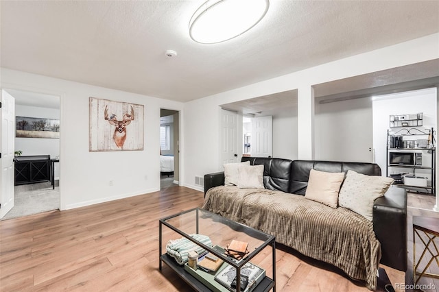 living room featuring baseboards, visible vents, light wood-style flooring, and a textured ceiling