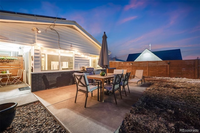 patio terrace at dusk with outdoor dining area and a fenced backyard