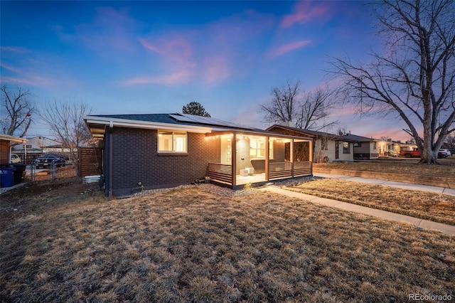 view of front of property with a porch, brick siding, fence, a yard, and roof mounted solar panels