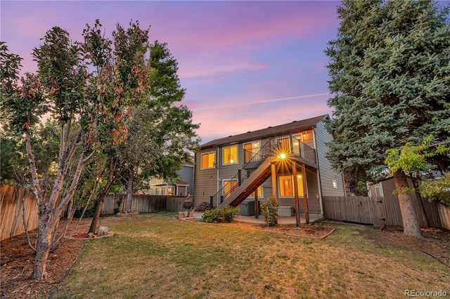 back of property at dusk featuring stairway, central AC unit, a fenced backyard, a yard, and a patio area