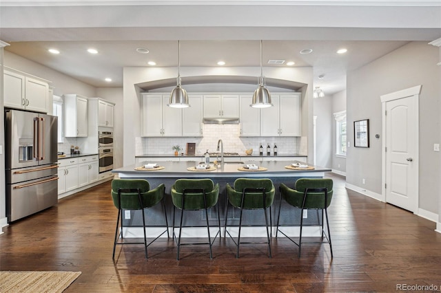 kitchen with a center island with sink, white cabinets, hanging light fixtures, and stainless steel appliances