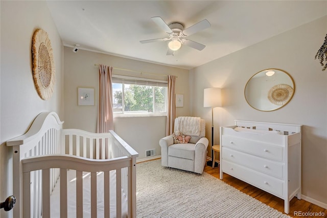 bedroom with ceiling fan, hardwood / wood-style flooring, and a nursery area