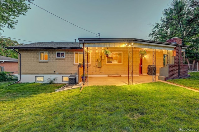 back house at dusk featuring a patio area, a yard, and central air condition unit