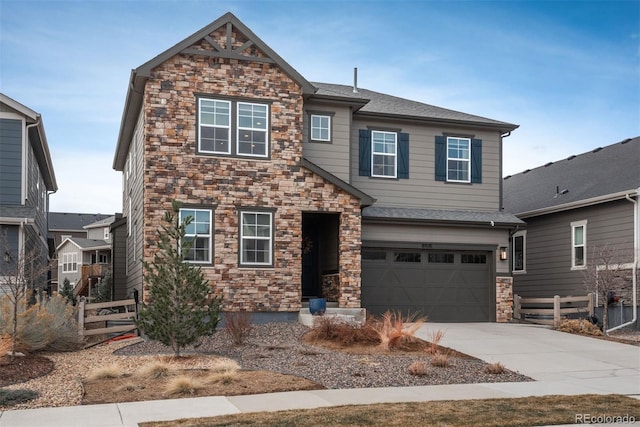 view of front of home featuring roof with shingles, concrete driveway, an attached garage, fence, and stone siding