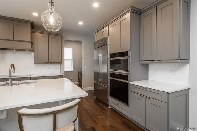 kitchen featuring stainless steel appliances, gray cabinets, a sink, and backsplash