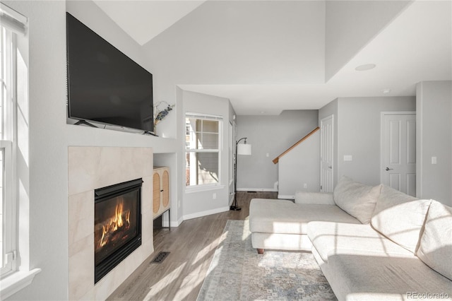 living area with lofted ceiling, visible vents, stairway, wood finished floors, and a tile fireplace