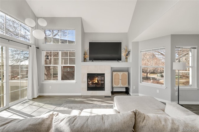 living area featuring high vaulted ceiling, a tile fireplace, plenty of natural light, and baseboards