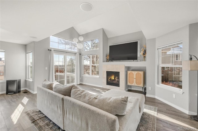 living area with a fireplace, baseboards, vaulted ceiling, and wood finished floors