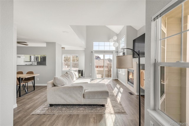 living area with high vaulted ceiling, baseboards, and wood finished floors