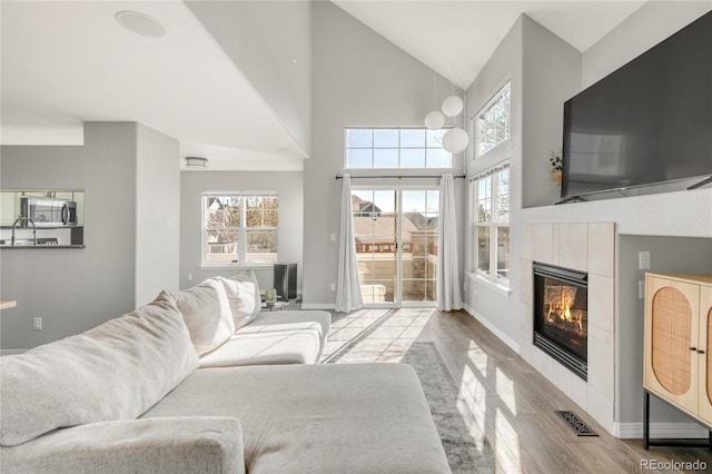 living room with visible vents, a tiled fireplace, wood finished floors, high vaulted ceiling, and baseboards