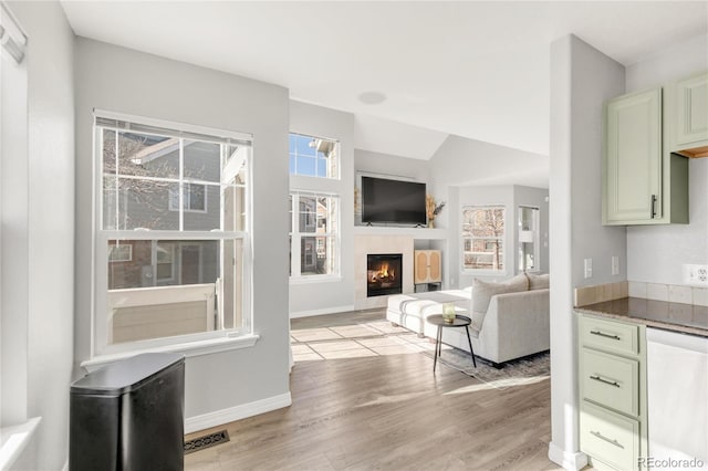 living area with visible vents, vaulted ceiling, light wood-type flooring, baseboards, and a tile fireplace