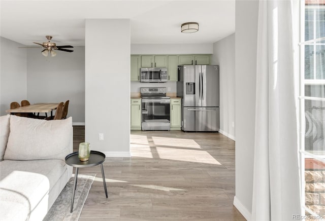 kitchen featuring appliances with stainless steel finishes, green cabinetry, light wood-style floors, and baseboards