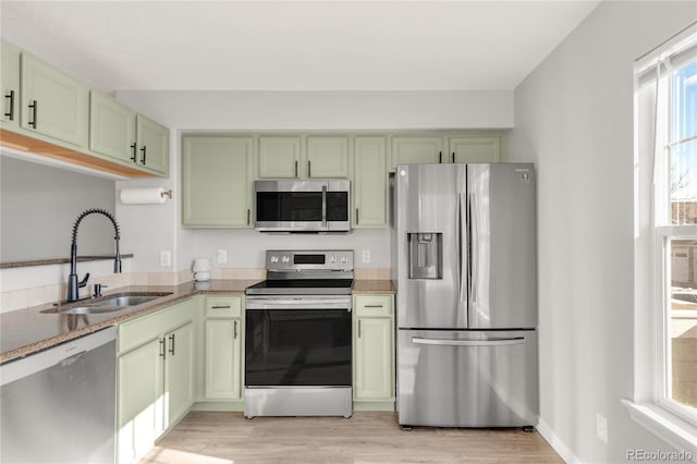 kitchen with appliances with stainless steel finishes, a sink, light wood finished floors, and green cabinets