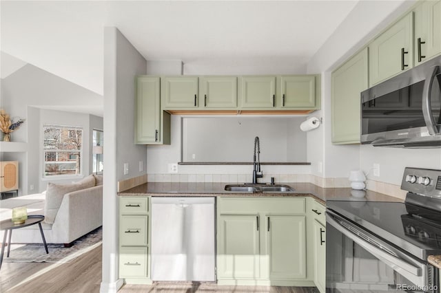 kitchen with stainless steel appliances, dark countertops, light wood-style flooring, a sink, and green cabinetry