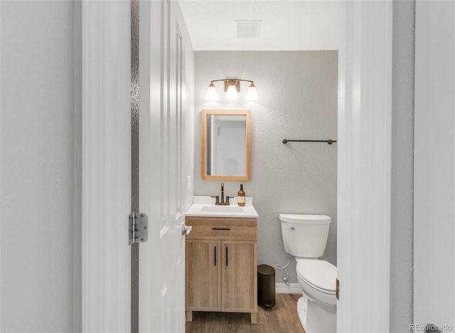 bathroom featuring toilet, wood finished floors, vanity, visible vents, and baseboards