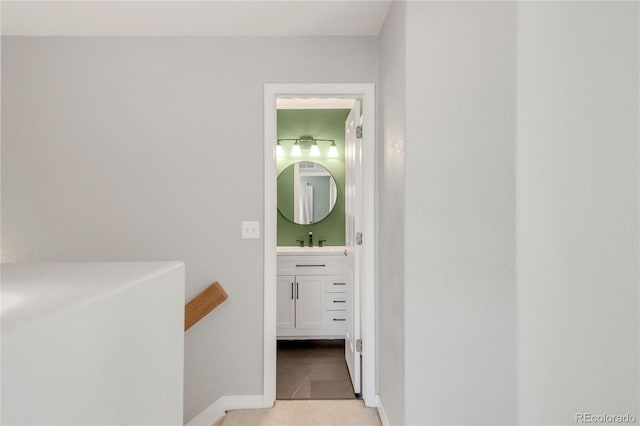 hall with carpet, a sink, and baseboards