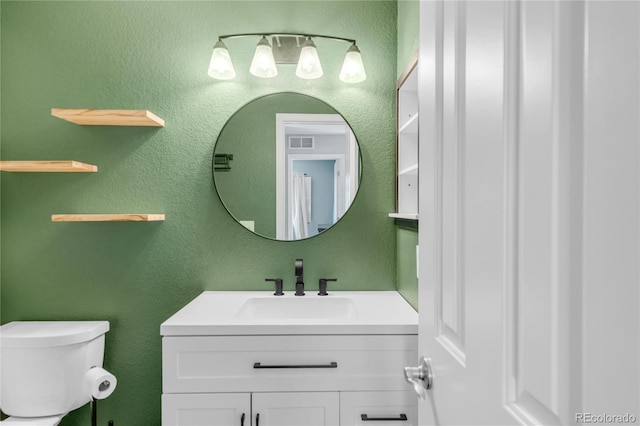 bathroom featuring visible vents, a textured wall, vanity, and toilet