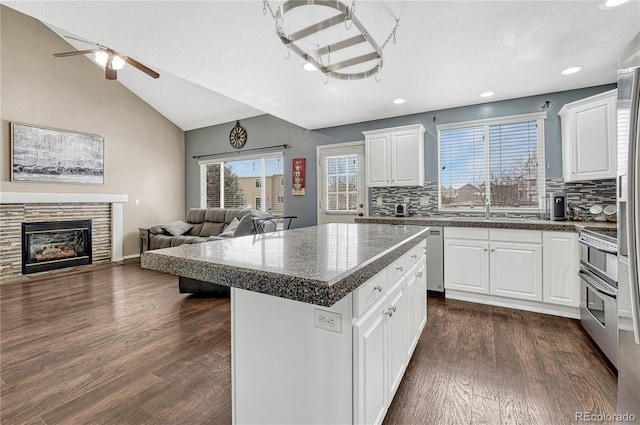 kitchen with white cabinetry, a stone fireplace, backsplash, lofted ceiling, and a kitchen island