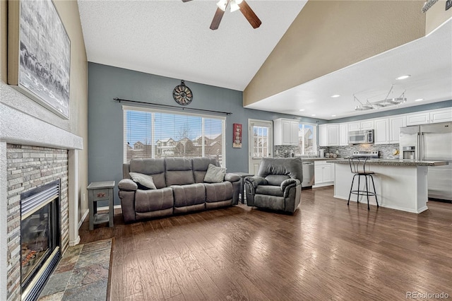 living room with a brick fireplace, a textured ceiling, ceiling fan, dark hardwood / wood-style floors, and lofted ceiling