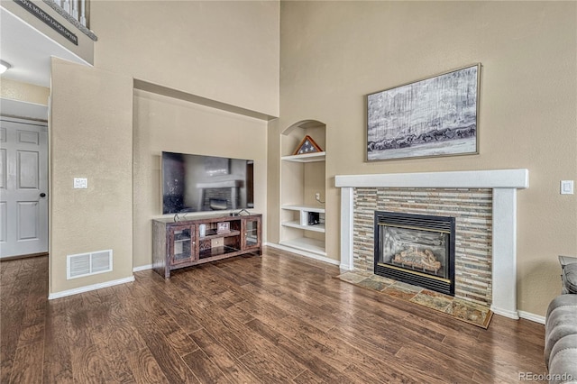 living room featuring built in features, a fireplace, and dark wood-type flooring