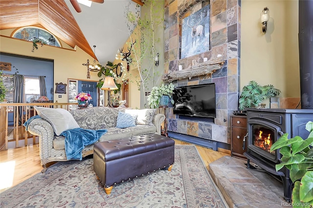 living area featuring ceiling fan, a wood stove, a glass covered fireplace, wood finished floors, and vaulted ceiling