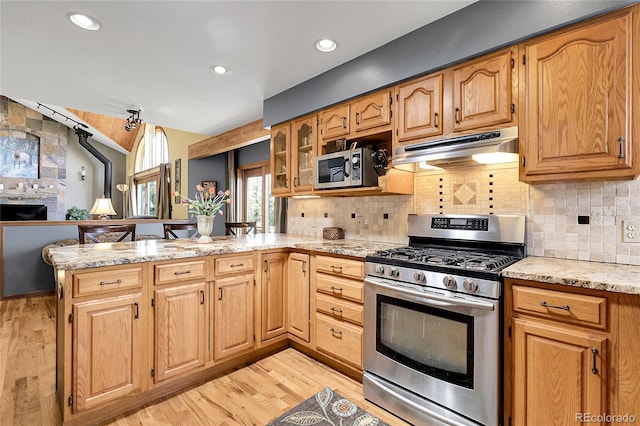 kitchen featuring appliances with stainless steel finishes, light wood-style flooring, a peninsula, tasteful backsplash, and under cabinet range hood