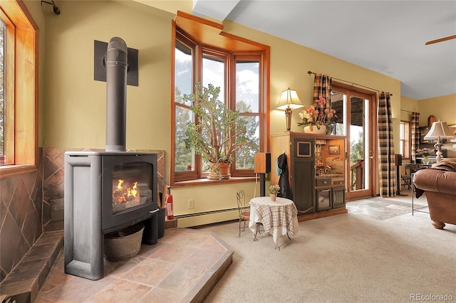 living area featuring a wood stove, carpet flooring, baseboard heating, and a healthy amount of sunlight