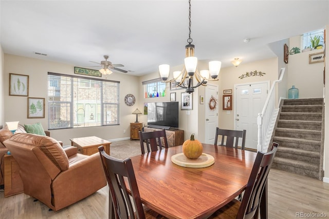 dining space with ceiling fan with notable chandelier and light wood-type flooring