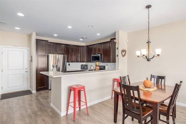 kitchen with hanging light fixtures, light hardwood / wood-style flooring, a kitchen bar, kitchen peninsula, and stainless steel appliances