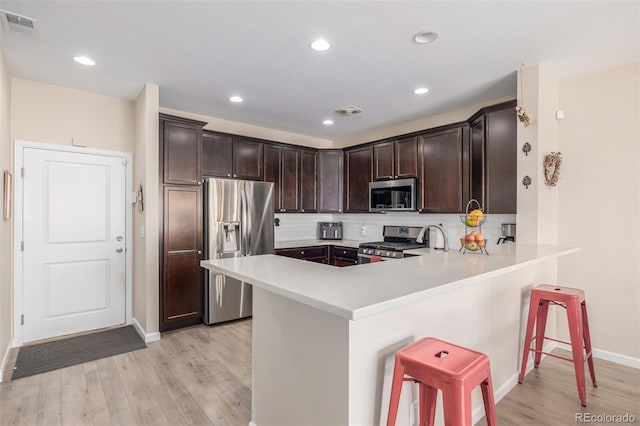 kitchen with a kitchen breakfast bar, kitchen peninsula, stainless steel appliances, and light hardwood / wood-style floors