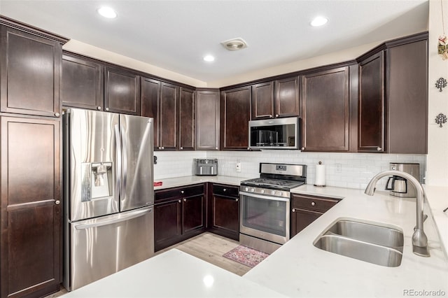 kitchen with sink, backsplash, light hardwood / wood-style floors, dark brown cabinets, and appliances with stainless steel finishes