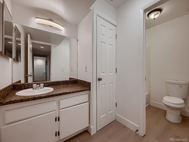 bathroom with toilet, vanity, baseboards, and wood finished floors